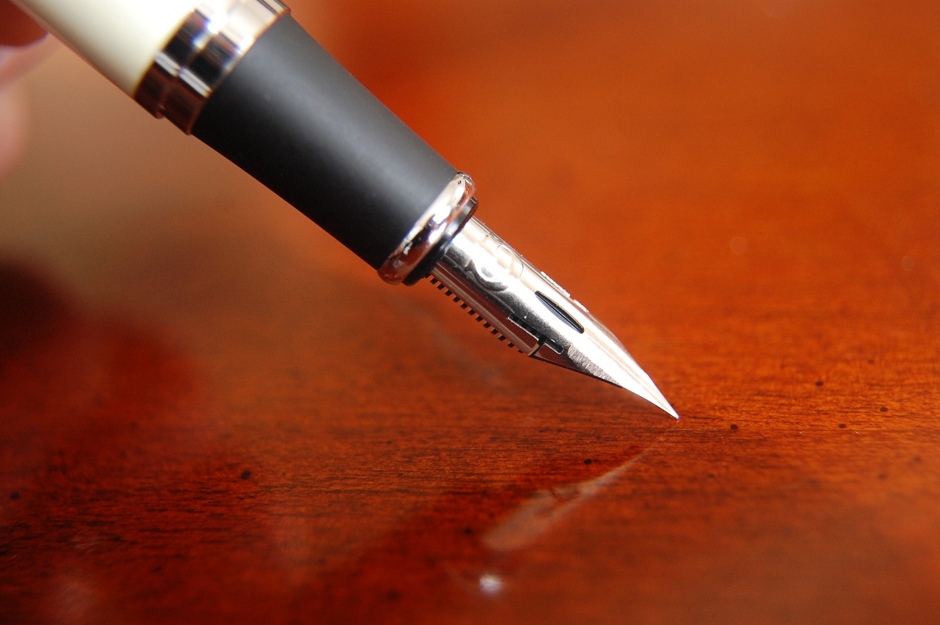 A fountain pen nib is shown over a brown wood surface